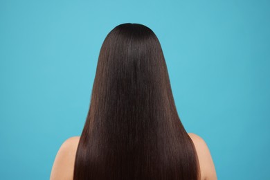 Woman with healthy hair after treatment on light blue background, back view