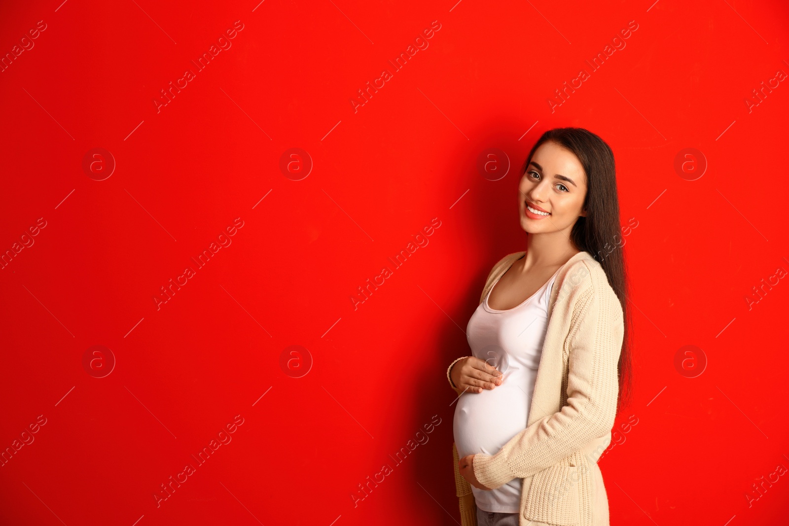 Photo of Happy pregnant woman on red background, space for text. Expecting baby