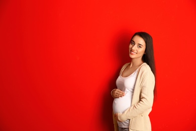 Happy pregnant woman on red background, space for text. Expecting baby