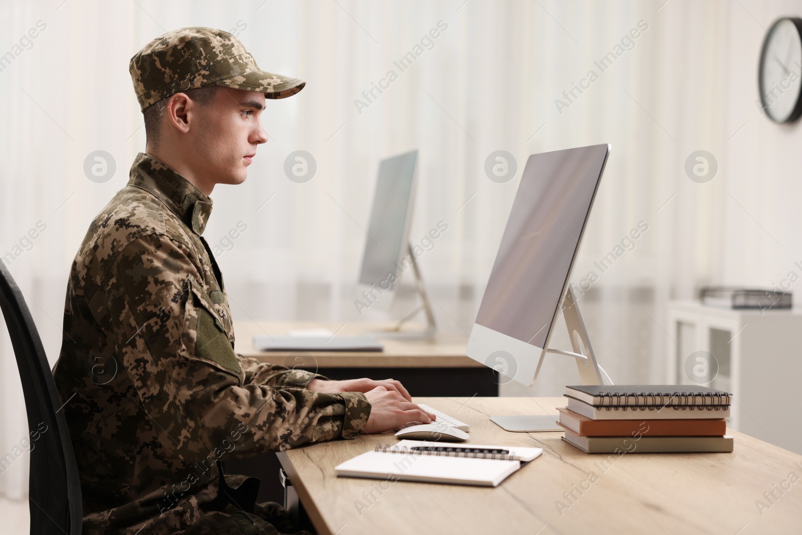 Photo of Military service. Young soldier working with computer at wooden table in office