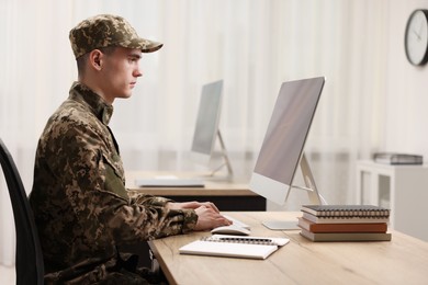 Photo of Military service. Young soldier working with computer at wooden table in office