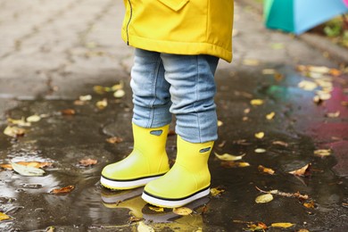 Photo of Little girl standing in puddle outdoors, closeup