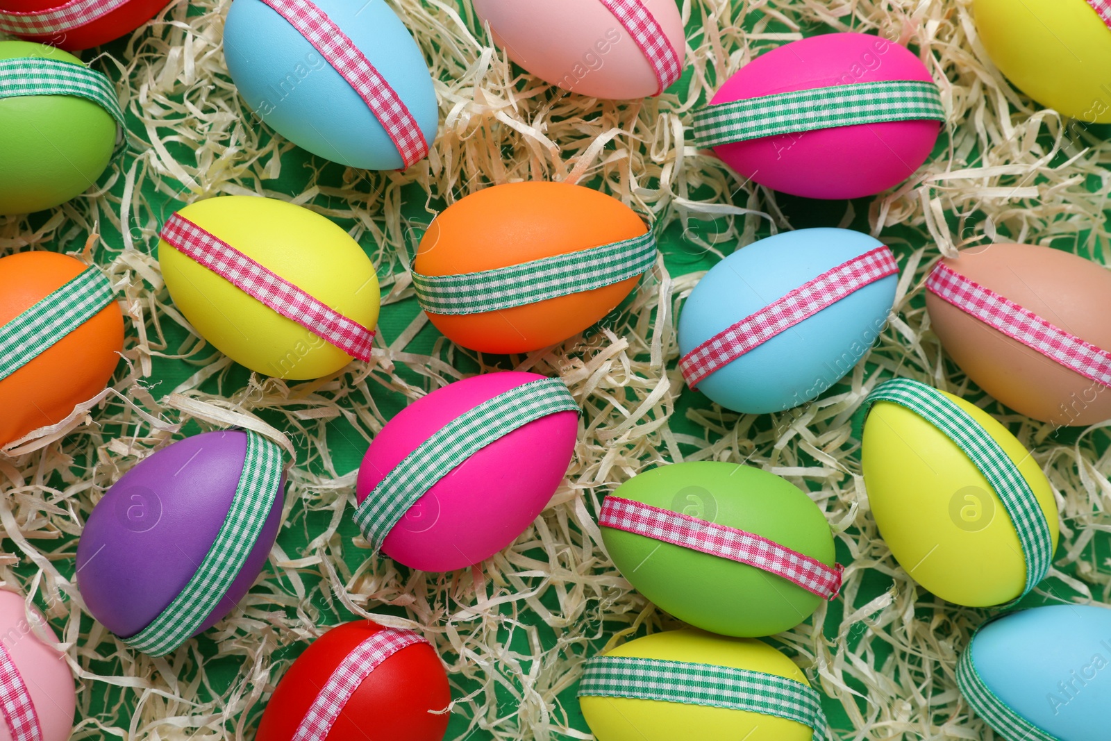 Photo of Festively decorated Easter eggs in paper filler on green background, flat lay