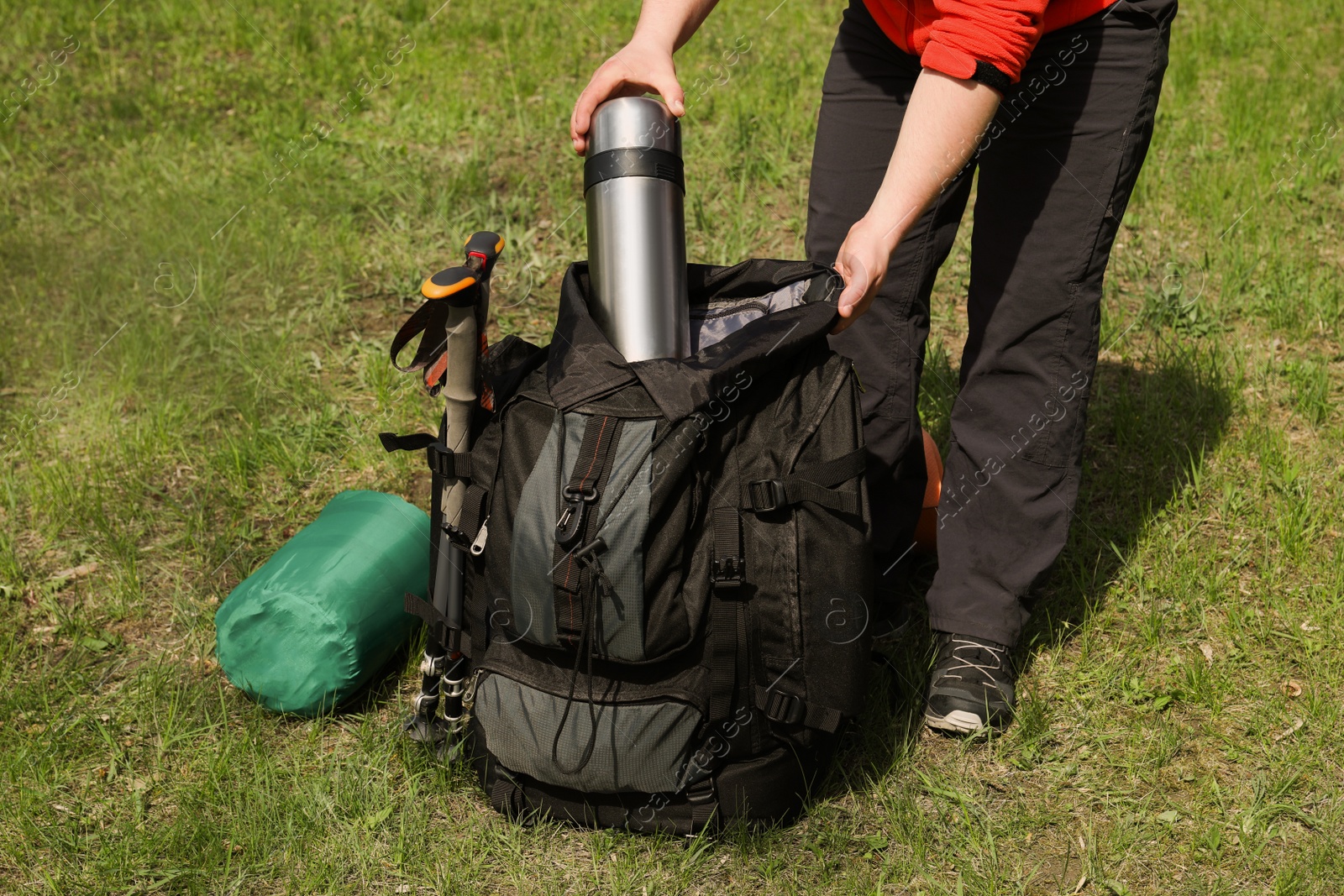 Photo of Hiker putting thermos into backpack outdoors, closeup