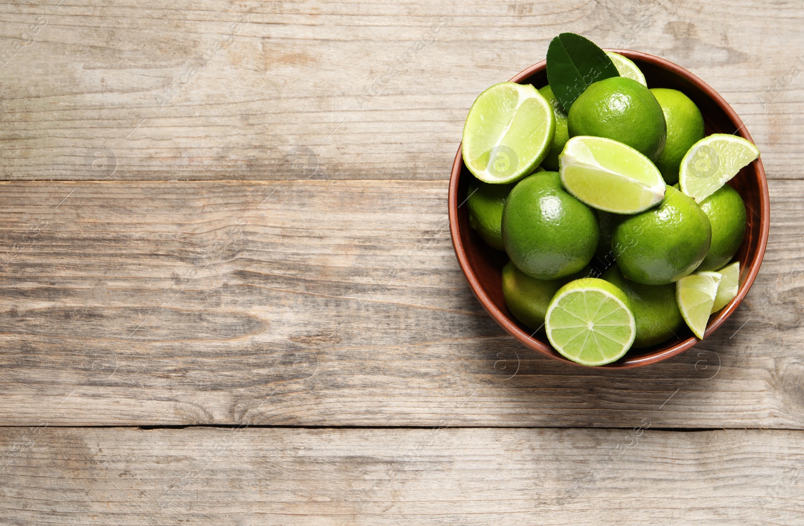 Photo of Tasty ripe limes in bowl on wooden table, top view. Space for text