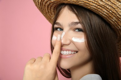 Teenage girl applying sun protection cream on her face against pink background, closeup