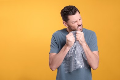 Man popping bubble wrap on yellow background, space for text. Stress relief