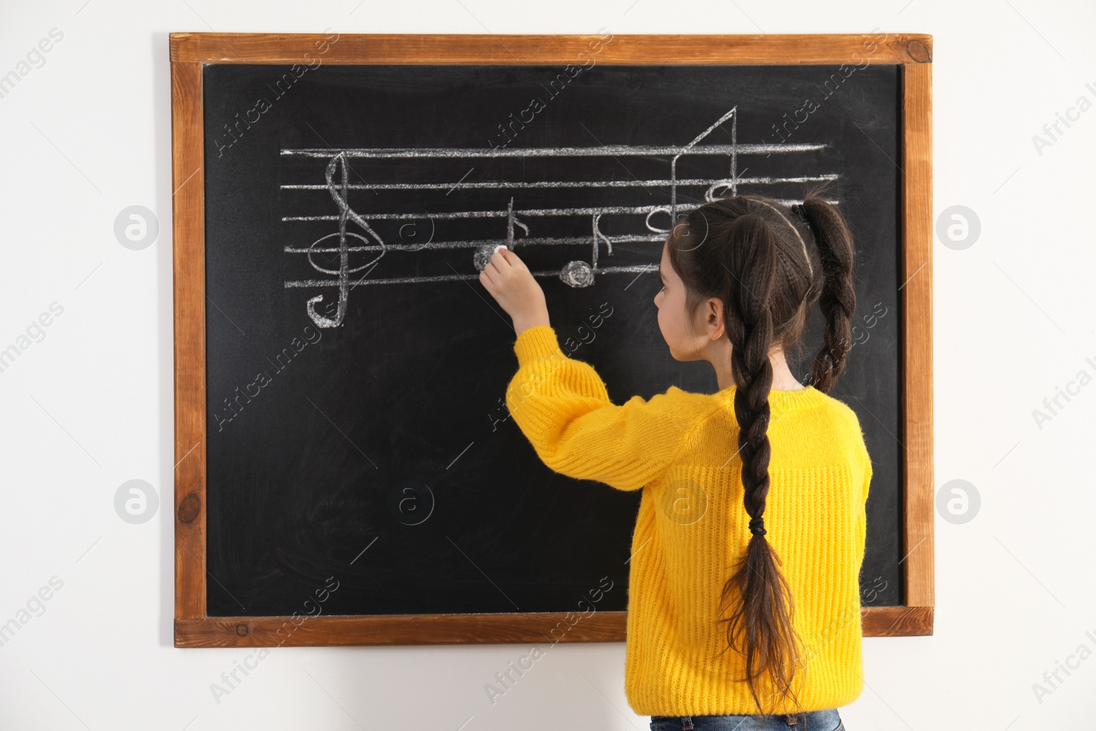 Photo of Little girl writing music notes on blackboard in classroom