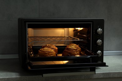 Photo of Open electric oven with delicious pastry on grey table indoors