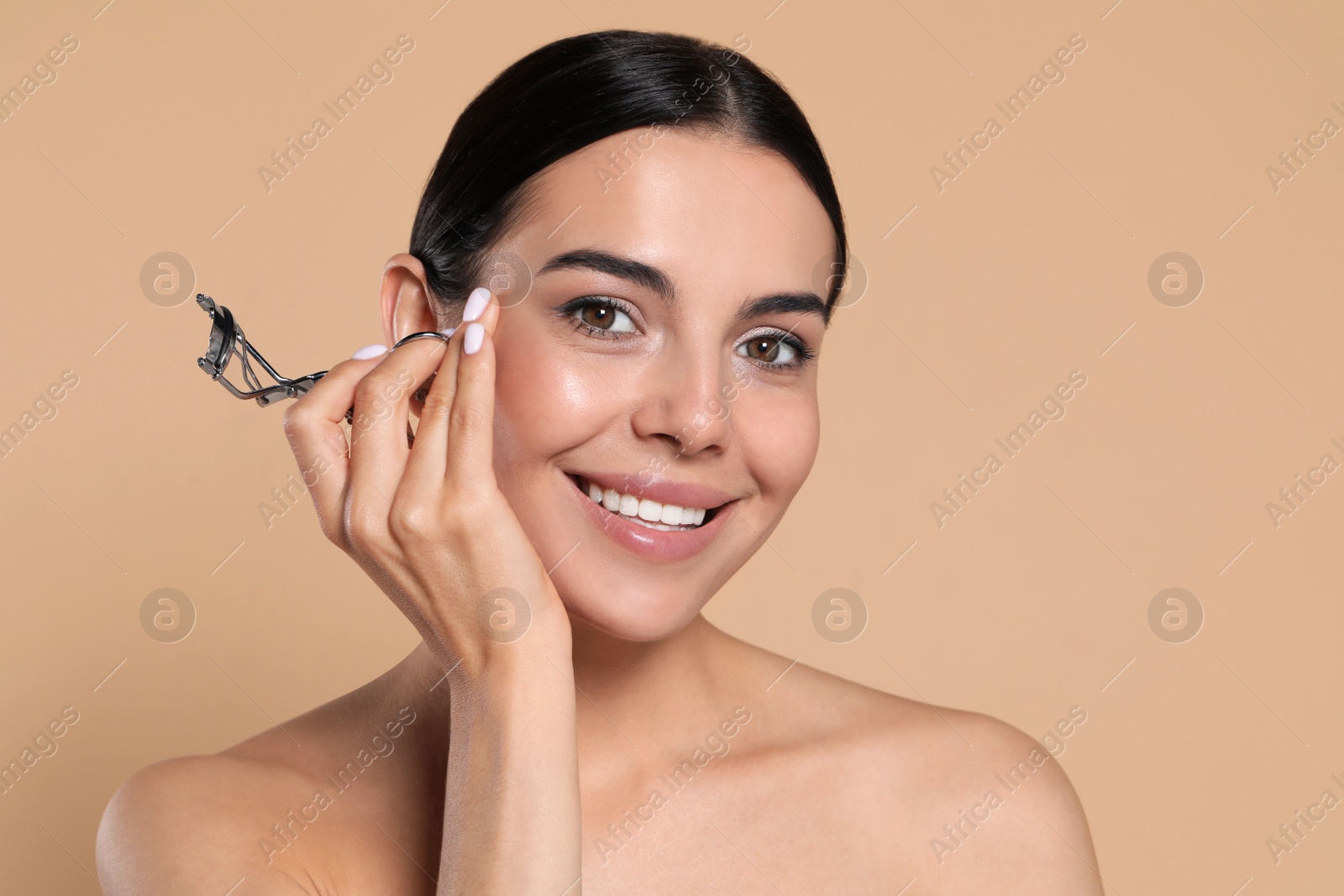 Photo of Beautiful young woman with eyelash curler on beige background