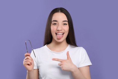 Photo of Happy woman showing tongue cleaner on violet background