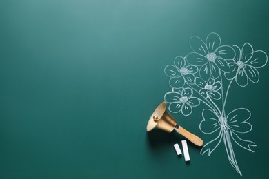 Photo of Golden bell, pieces of chalk and drawn flowers on green board, flat lay. School time