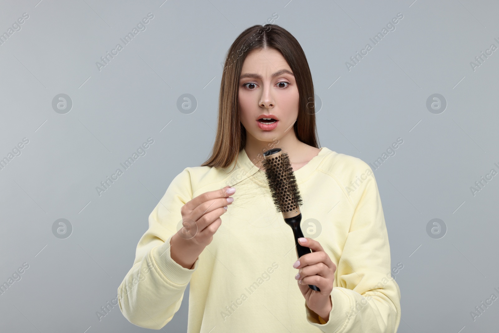 Photo of Emotional woman untangling her lost hair from brush on light grey background. Alopecia problem