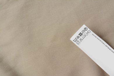 Photo of White clothing label with care information on beige garment, top view. Space for text