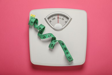 Bathroom scale and measure tape on pink background, top view