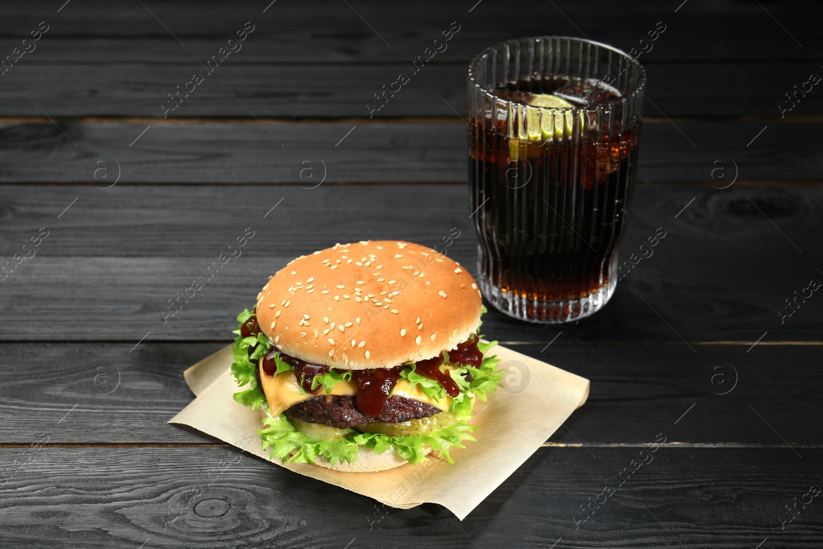 Photo of Burger with delicious patty and soda drink on black wooden table