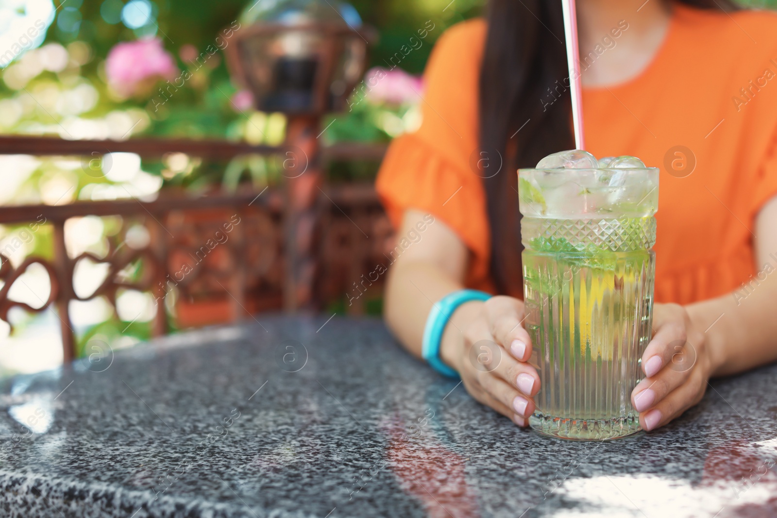 Photo of Young woman with glass of tasty lemonade at table in cafe, outdoors. Natural detox drink