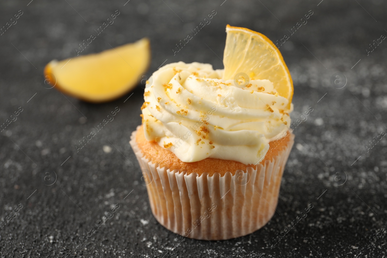 Photo of Tasty cupcake with cream, zest and lemon slice on black textured table, closeup