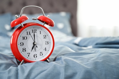 Photo of Analog alarm clock on bed. Time of day