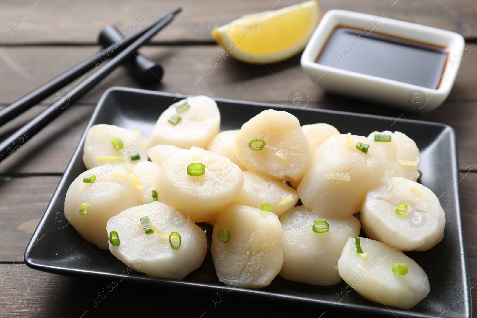 Photo of Raw scallops with green onion on wooden table, closeup