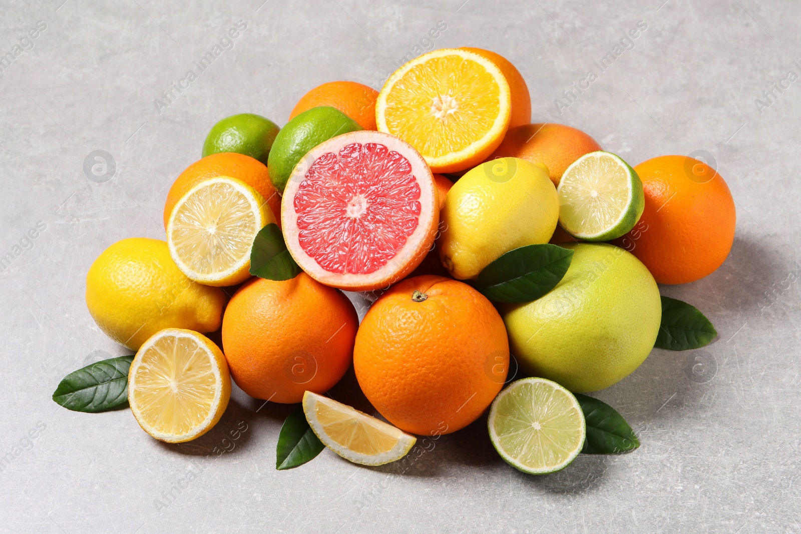 Photo of Pile of different fresh citrus fruits and leaves on grey textured table, closeup