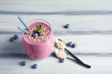 Photo of Tasty blueberry smoothie in glass, berries and oatmeal on wooden table