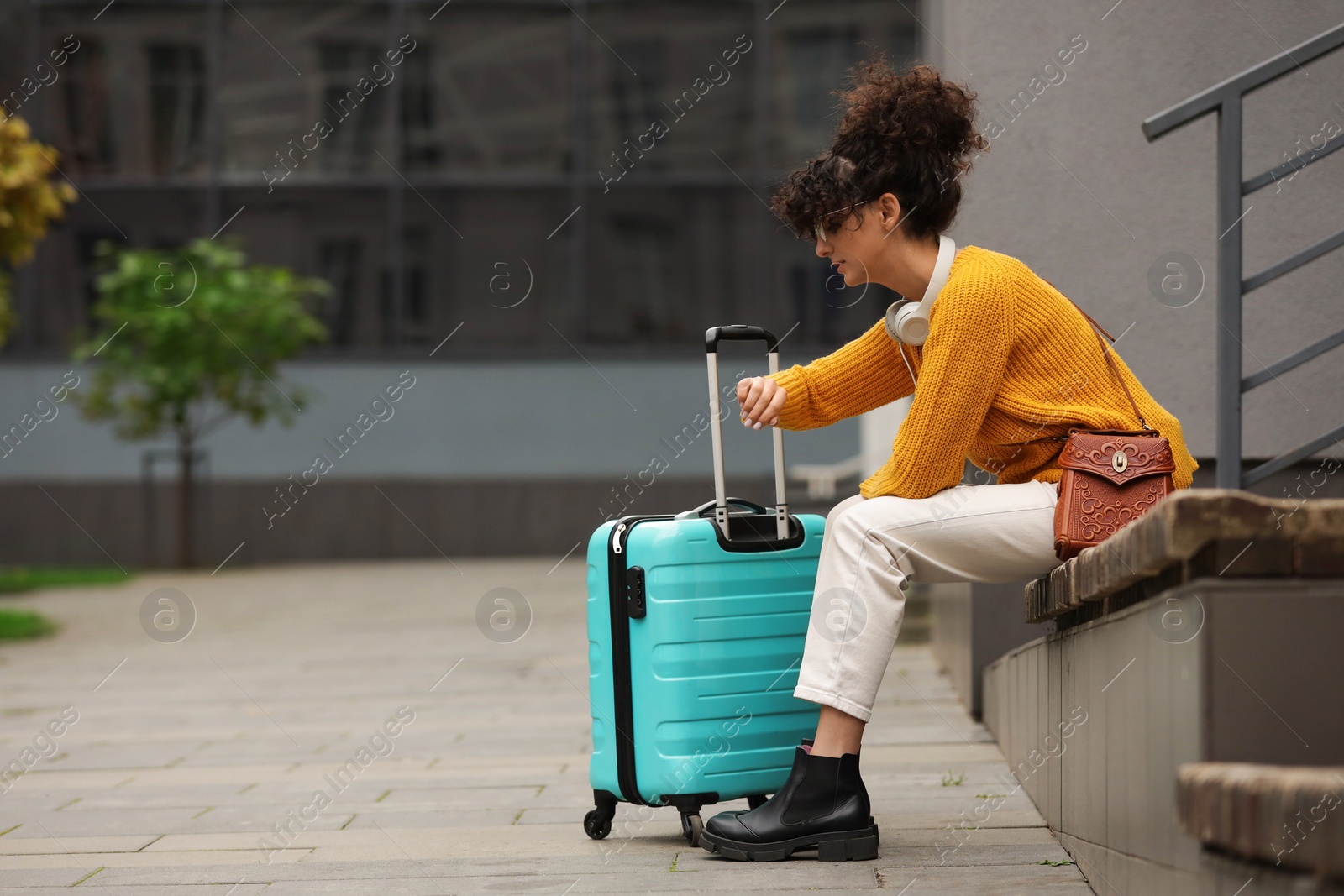 Photo of Being late. Worried woman with suitcase looking at watch on bench outdoors, space for text