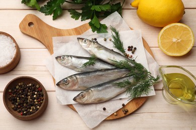 Photo of Fresh raw sprats, peppercorns and dill on light wooden table, flat lay