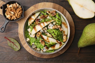 Photo of Delicious pear salad with sauce in bowl and ingredients on wooden table, flat lay