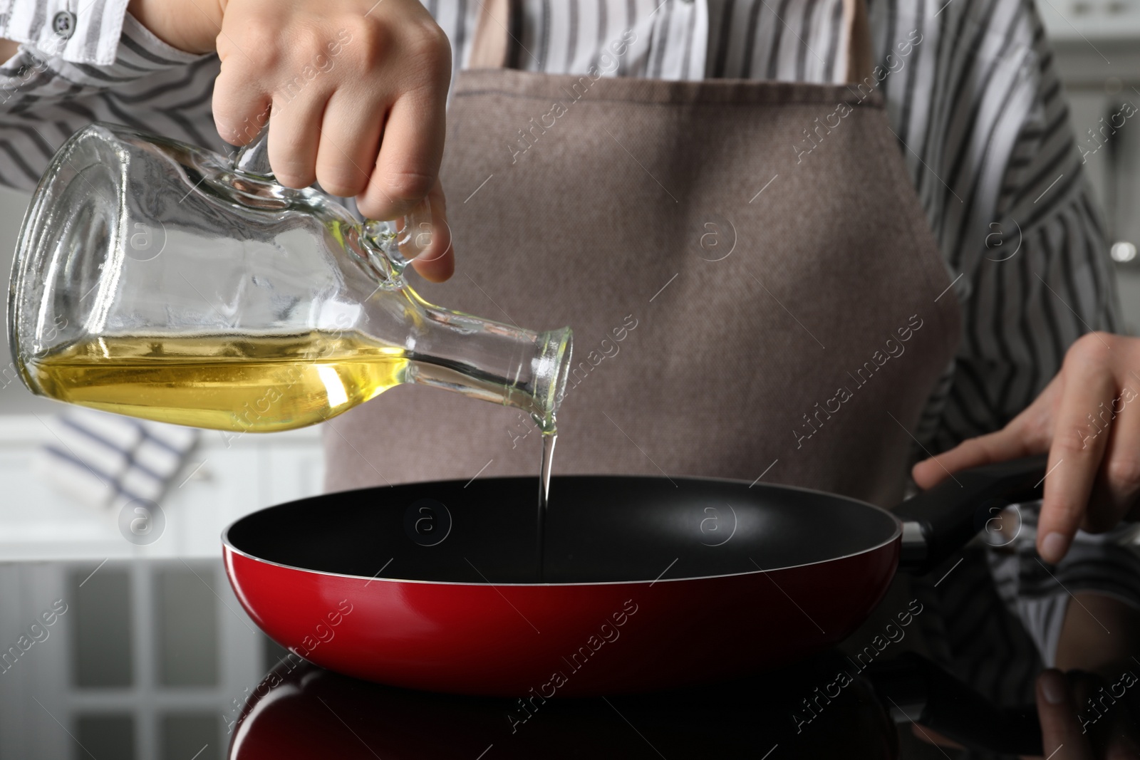 Photo of Woman pouring cooking oil from jug into frying pan on stove, closeup