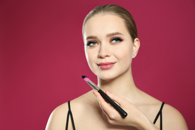 Artist applying makeup onto woman's face on pink background