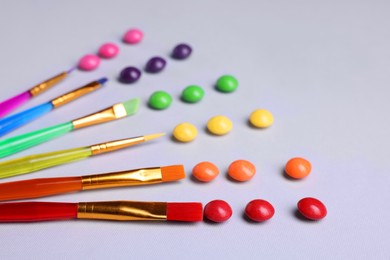 Photo of Creative composition with paint brushes and colorful candies on light grey background, closeup