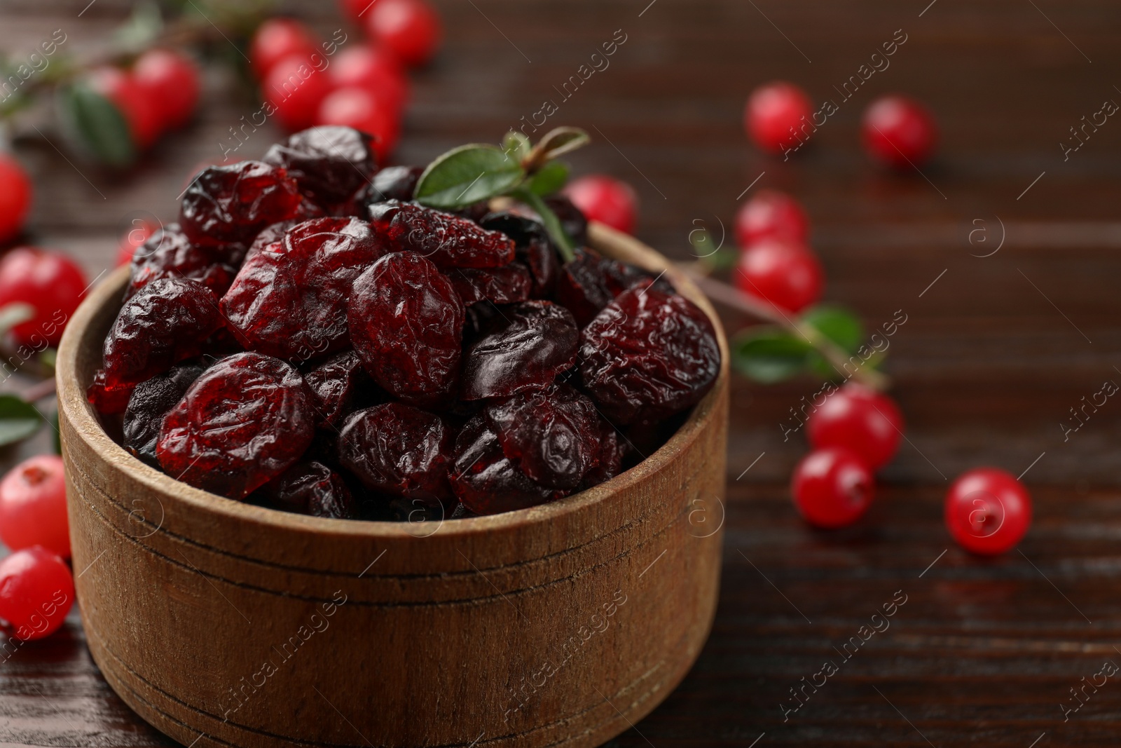 Photo of Tasty dried cranberries in bowl, fresh ones and leaves on wooden table, closeup. Space for text