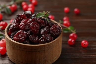 Photo of Tasty dried cranberries in bowl, fresh ones and leaves on wooden table, closeup. Space for text