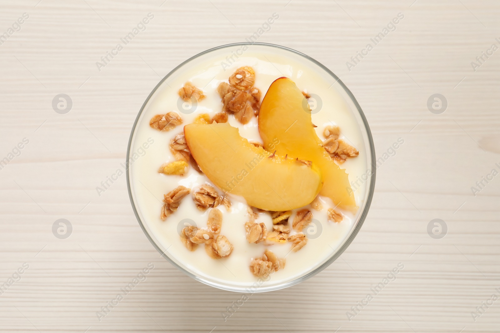 Photo of Tasty peach yogurt with granola and pieces of fruit in dessert bowl on white wooden table, top view