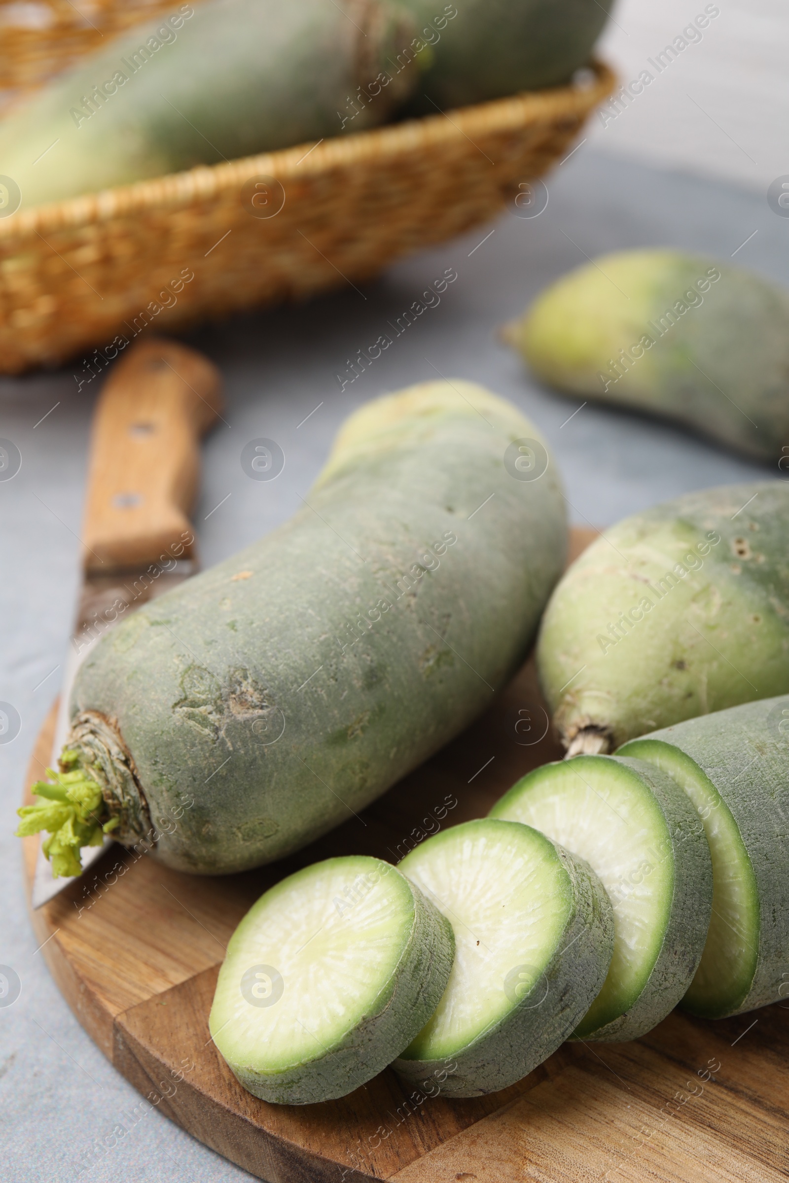Photo of Green daikon radishes and knife on light grey table, closeup