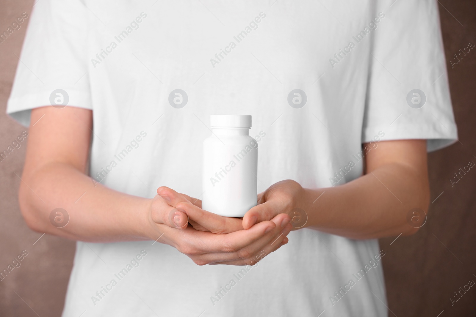 Photo of Woman holding blank white bottle with vitamin pills against light brown background, closeup