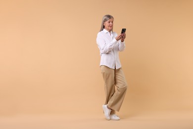 Photo of Senior woman with phone on beige background, space for text