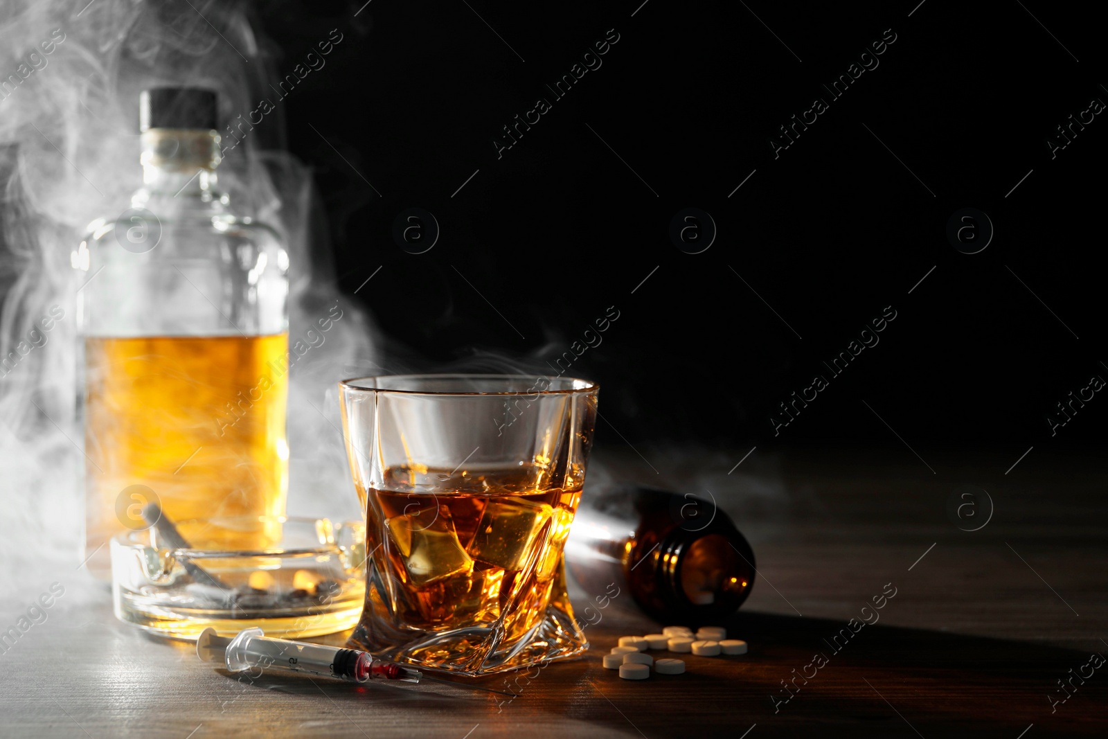 Photo of Alcohol and drug addiction. Whiskey in glass, syringe, pills and cigarettes on wooden table, space for text
