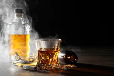 Alcohol and drug addiction. Whiskey in glass, syringe, pills and cigarettes on wooden table, space for text