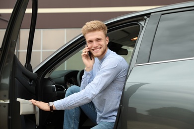Photo of Young handsome man talking on phone while opening car door
