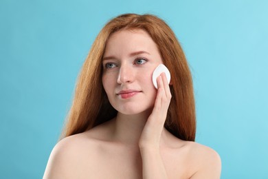 Beautiful woman with freckles wiping face on light blue background