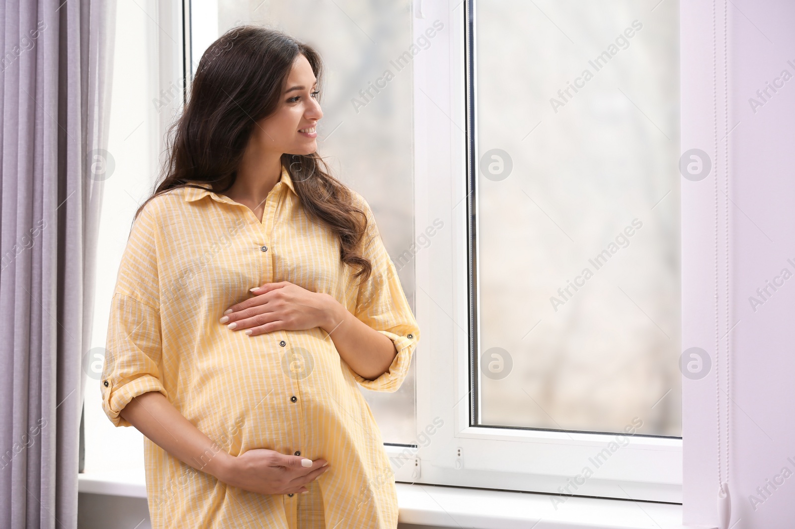 Photo of Beautiful pregnant woman near window at home