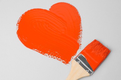 Photo of Heart shape made with orange paint and brush on white background