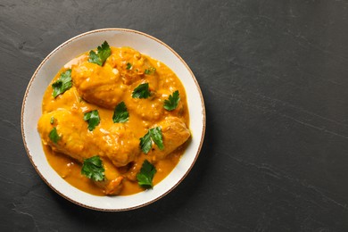 Tasty chicken curry with parsley on black textured table, top view. Space for text