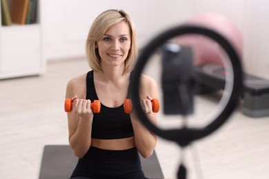 Smiling sports blogger working out with dumbbells while streaming online fitness lesson at home