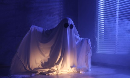 Photo of Creepy ghost. Woman covered with sheet near window in blue light