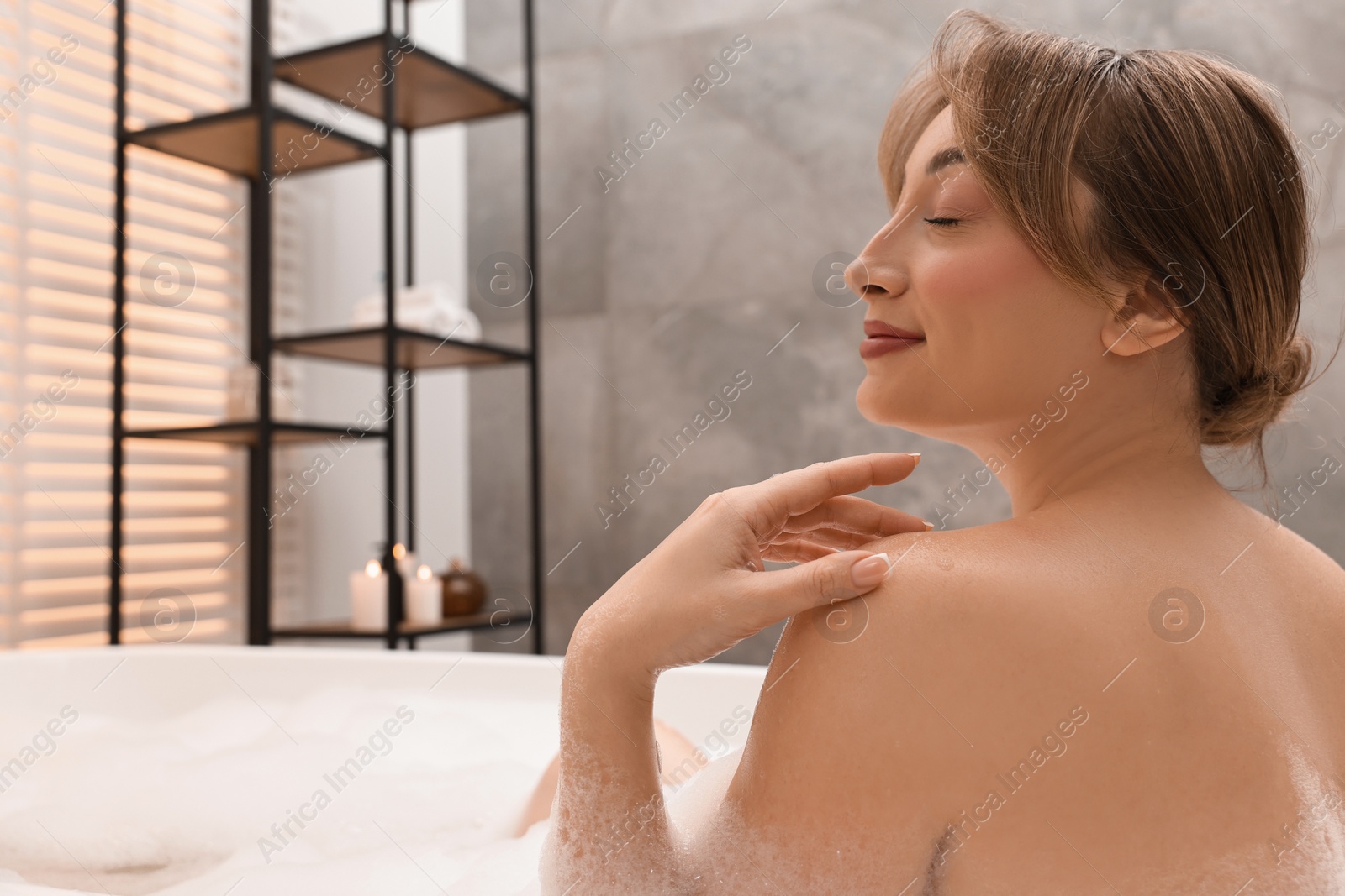 Photo of Happy woman taking bath with foam in tub indoors. Space for text