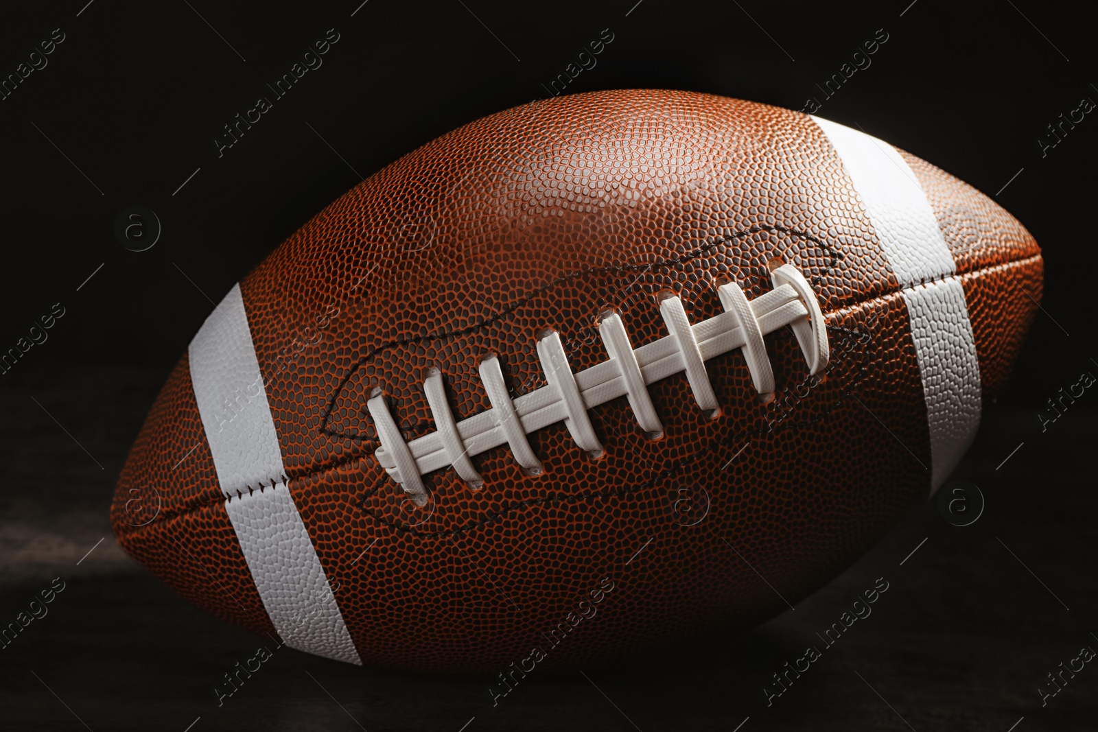 Photo of New American football ball on table against dark background