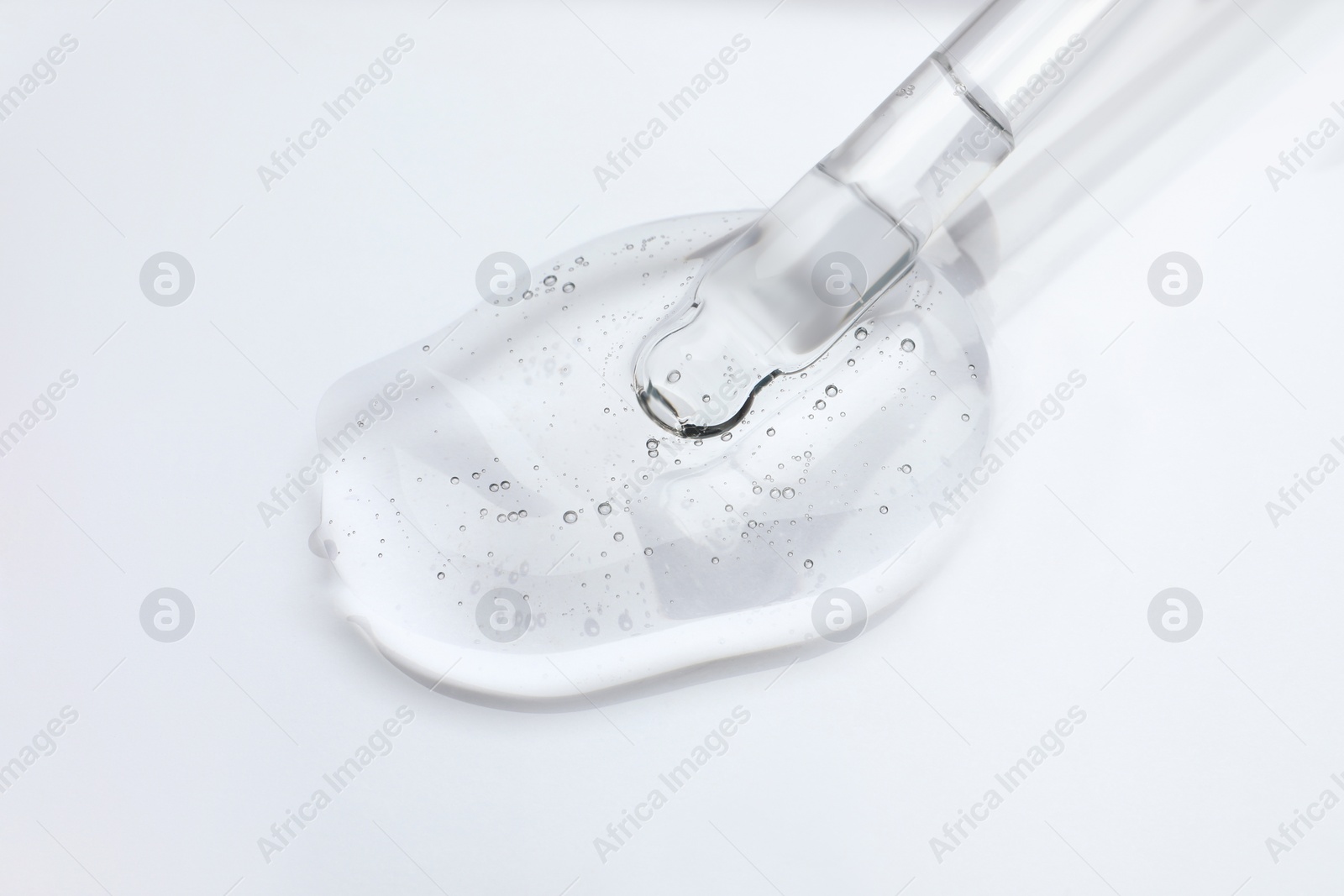 Photo of Dripping cosmetic oil from pipette onto light surface, closeup